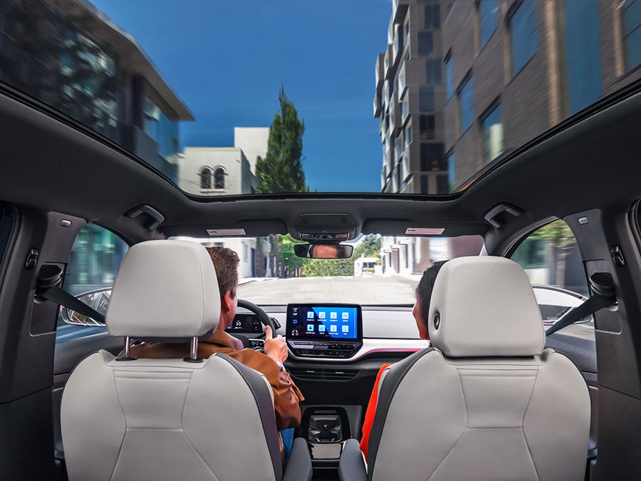 A forward shot of a man and woman driving an ID.4 with the sunshade open as they head down an urban street.