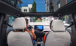 A forward facing shot of an ID.4 with focus on the driver and passenger seats, center console display, and available panoramic sunroof.