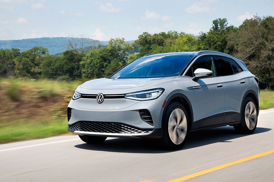 An ID.4 in Moonstone Gray drives along a highway with trees and mountains in the background.