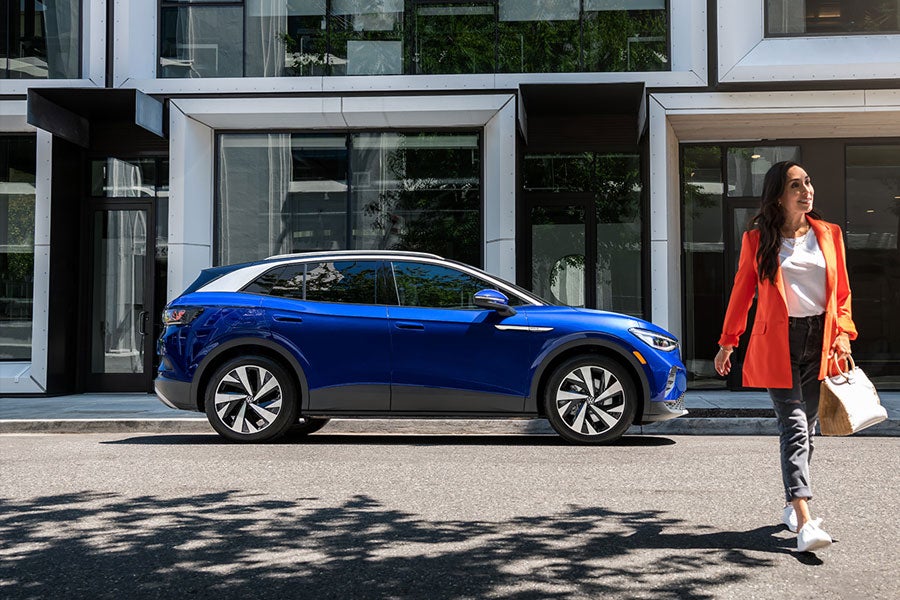 A woman walks away from an ID.4 in Dusk Blue Metallic that’s parked on an urban street.