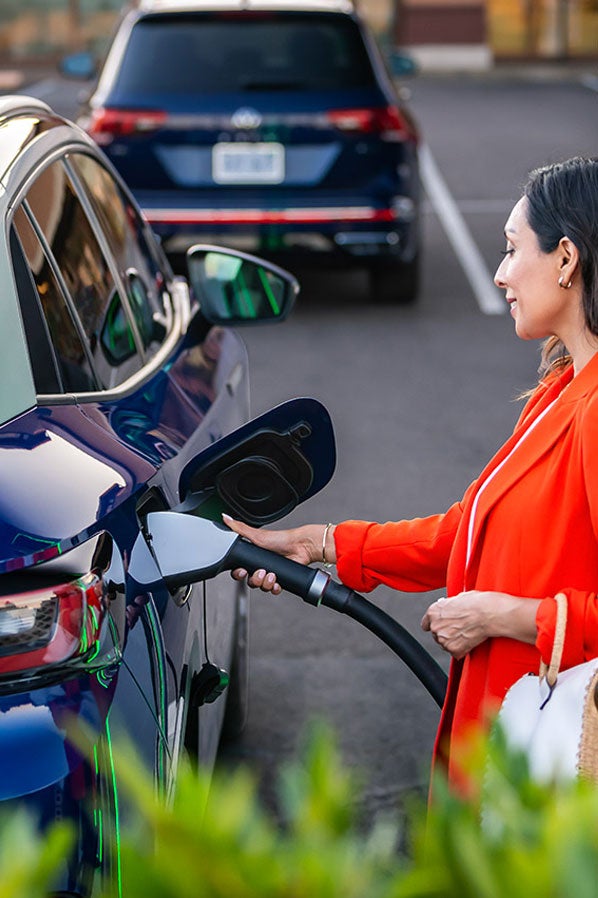 A well-dressed woman, parked at charging station stands on the passenger side of an ID.4 in Dusk Blue Metallic as she plugs in the car.
