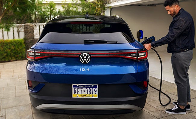 A man charges an ID.4 (in Dusk Blue Metallic) in a residential driveway.