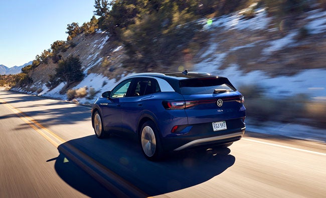 A ¾ rear shot of an ID.4 in Dusk Blue Metallic speeds up a two-lane highway in a mountain setting.